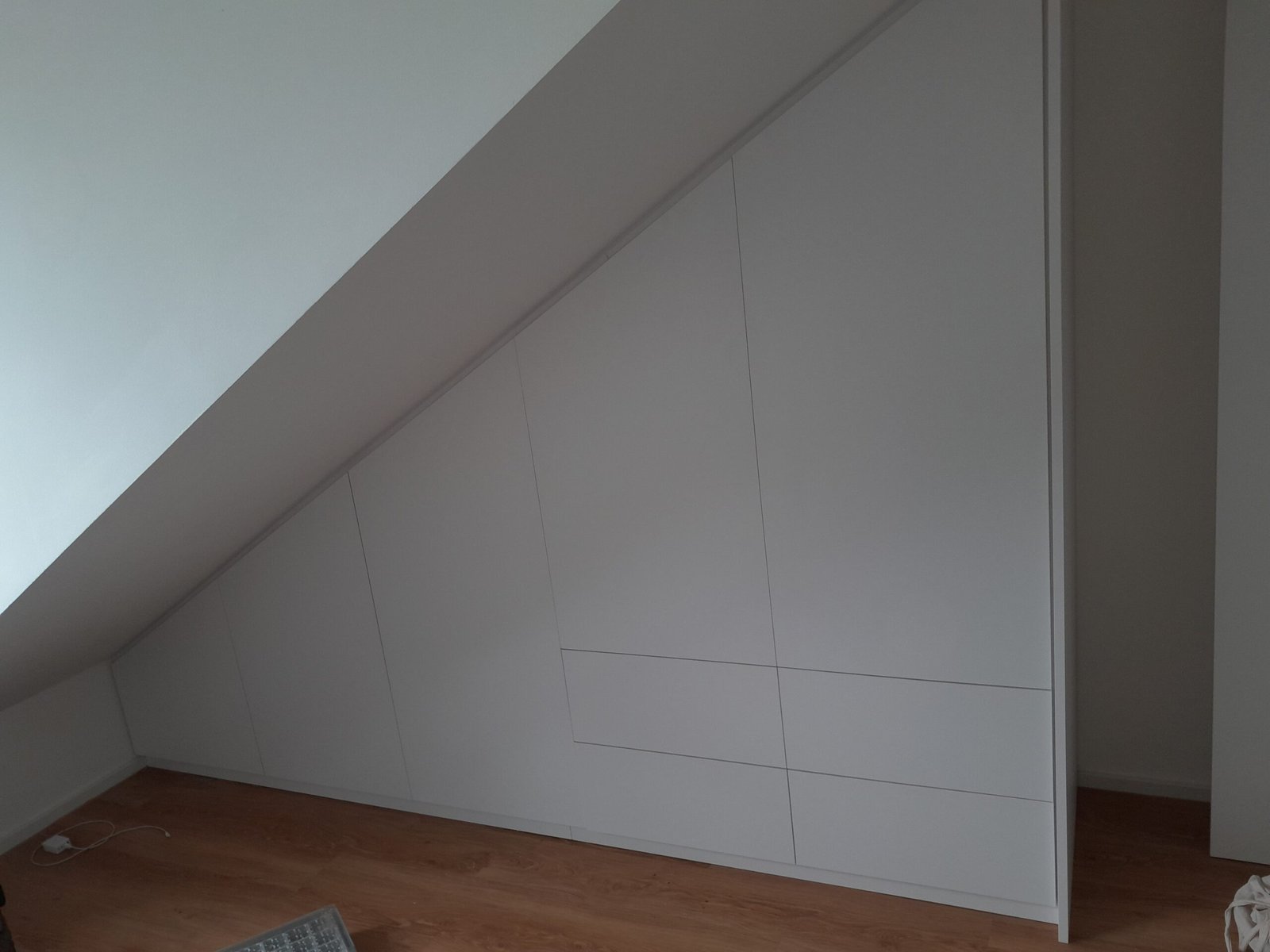 Weißer Einbauschrank unter einer Dachschräge, grifflose Türen und Schubkästen