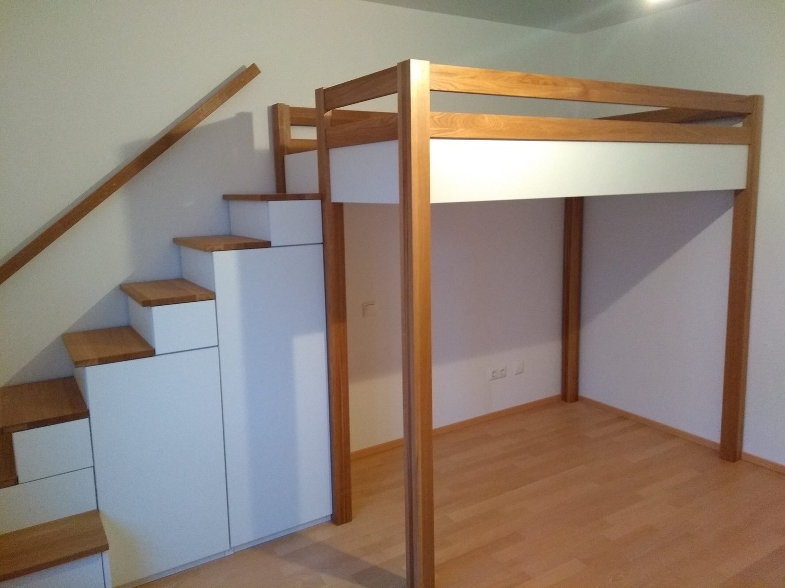 Hochbett mit Holzrahmen, daneben ein weißer Treppenschrank mit Holzstufen