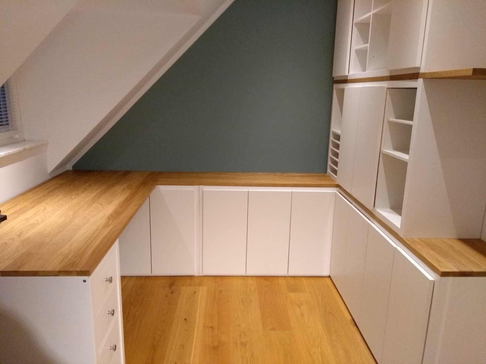 Weiße Schrankzeile unter einer Dachschräge mit Abdeckplatten aus Eiche
